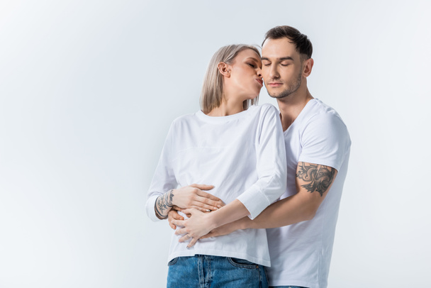 young tattooed pregnant woman kissing husband isolated on grey - Fotoğraf, Görsel