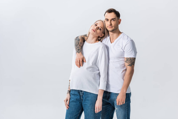 fiatal tetovált terhes nő átöleli férjjel elszigetelt szürke - Fotó, kép