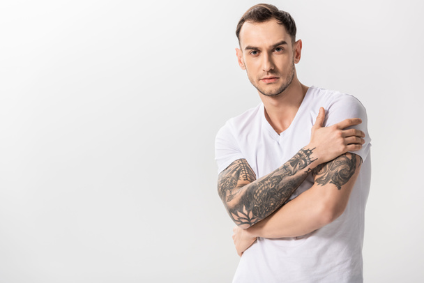 σοβαρός όμορφος νεαρός άνδρας με τατουάζ με σταυρωμένα χέρια απομονωμένος στα λευκά - Φωτογραφία, εικόνα
