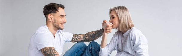 young tattooed pregnant woman kissing husband hand isolated on grey, panoramic shot - Fotografie, Obrázek