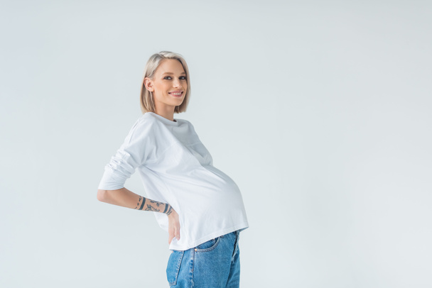 side view of happy young tattooed pregnant woman isolated on grey - Photo, Image