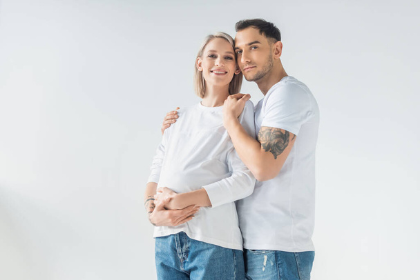 happy young tattooed pregnant woman hugging with boyfriend isolated on grey - Zdjęcie, obraz