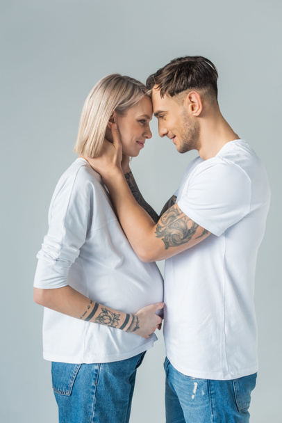side view of young tattooed pregnant woman with boyfriend isolated on grey - Foto, afbeelding