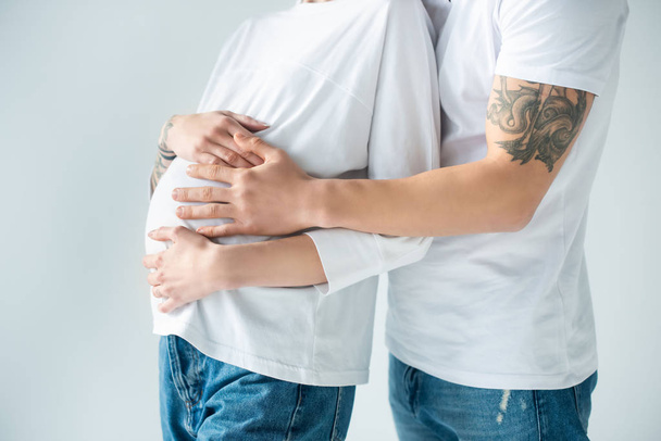 обрезанный вид молодой татуированной беременной женщины с парнем, изолированным на серой
 - Фото, изображение