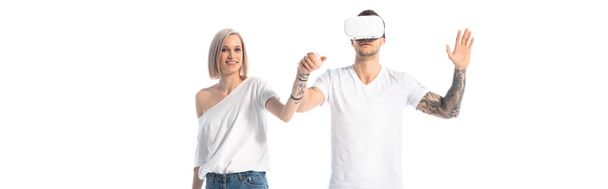 jong getatoeëerde man in vr headset in de buurt glimlachende vriendin geïsoleerd op wit, panoramisch schot - Foto, afbeelding