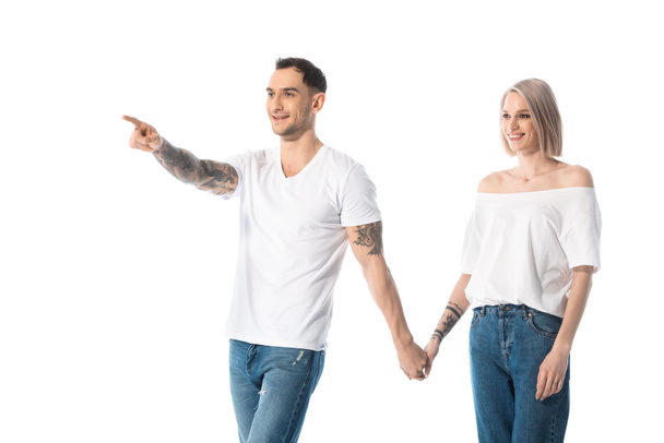 young tattooed couple holding hands while man pointing with finger away isolated on white - Φωτογραφία, εικόνα