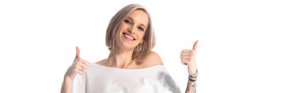 šťastný mladý tetovaný dívka ukazující palce nahoru izolované na bílém, panoramatický výstřel - Fotografie, Obrázek