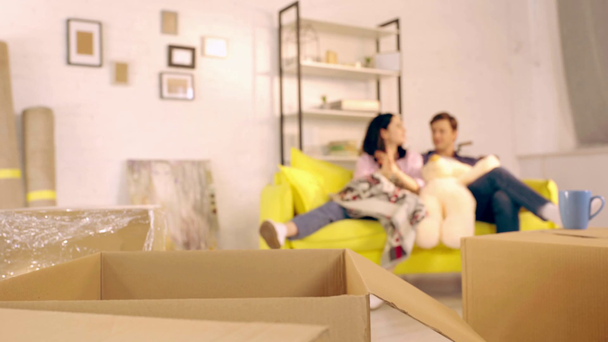 Επιλεκτική εστίαση των πακέτων και ζευγάρι στον καναπέ στο νέο σπίτι - Πλάνα, βίντεο