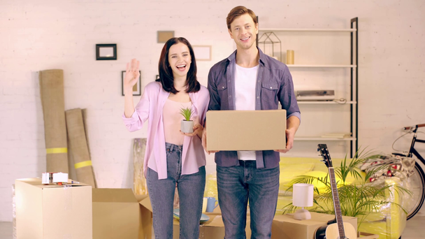 Χαρούμενο ζευγάρι με κουτί και φυτό στο νέο σπίτι - Πλάνα, βίντεο