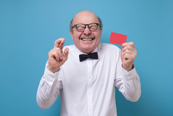 Senior latin man tenant une carte de crédit croisant les doigts pour avoir de la chance
 - Photo, image