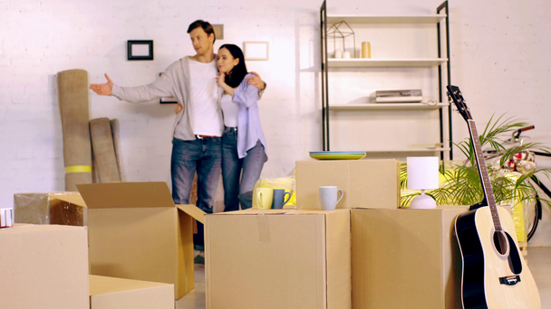 Young couple hugging and talking near boxes in new home - 映像、動画