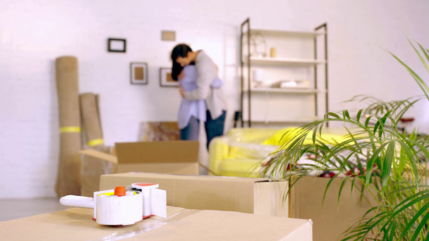 Selective focus of packing tape on box and couple hugging in new home - Video, Çekim