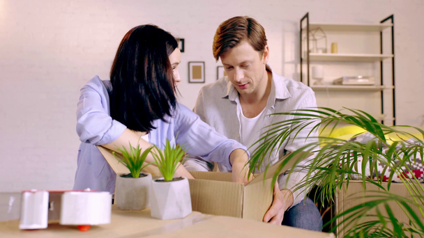 Couple talking and packing plants in box at home - Felvétel, videó