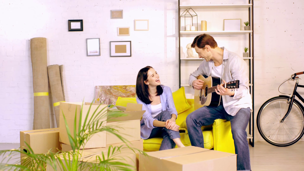 Koppel met akoestische gutar lachen in de buurt van dozen in nieuw huis - Video