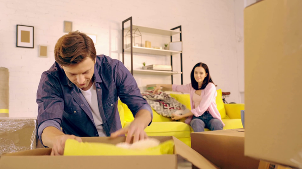 Muž vybalování polštář a kostkované z krabice poblíž přítelkyně na gauči - Záběry, video