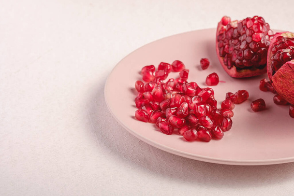 Verse smakelijke zoete geschilde granaatappel met rode zaden in roze plaat op witte achtergrond, hoek uitzicht, gezond voedsel fruit - Foto, afbeelding