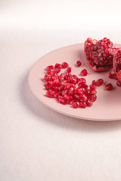Granada fresca pelada dulce sabrosa con semillas rojas en plato rosa sobre fondo blanco, vista angular, frutas saludables
 - Foto, Imagen