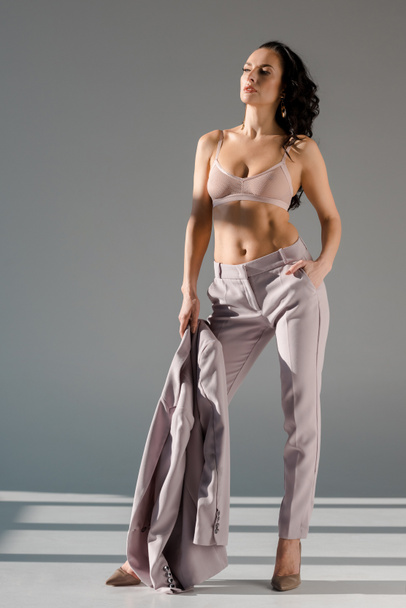 sexy and stylish woman in bra holding jacket on grey background  - Фото, зображення