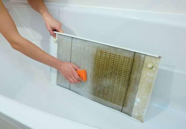 Donna pulizia cappa filtro nella vasca da bagno con spugna - Foto, immagini