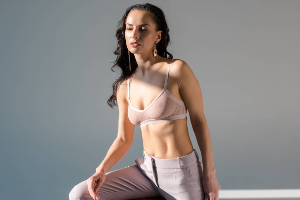 sexy woman in trousers and bra looking away on grey background  - Photo, Image