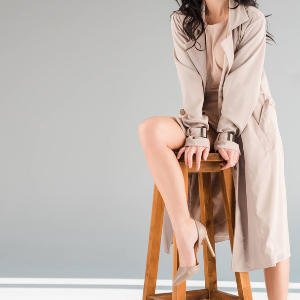 cropped view of woman in coat sitting on stool on grey background  - Valokuva, kuva