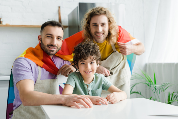 счастливые гомосексуальные мужчины с радужным флагом lgbt около веселой смешанной расы сына
  - Фото, изображение