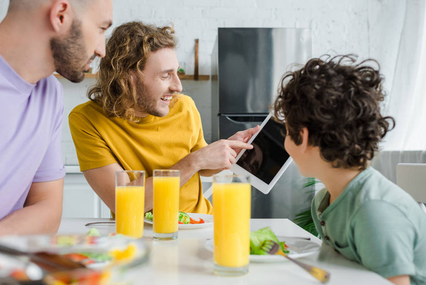 happy homosexual man pointing with finger at digital tablet with blank screen near mixed race son  - Photo, Image