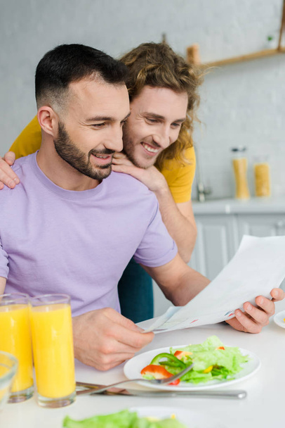happy homosexual men looking at drawing near salad and glasses with orange juice  - Photo, Image
