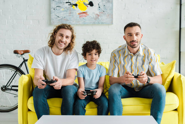 KYIV, UKRAINE - JANUARY 28, 2020: happy homosexual couple and mixed race kid playing video game  - Foto, immagini