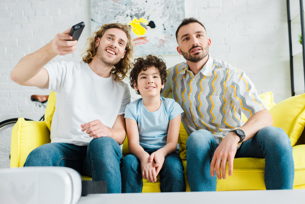 happy homosexual parents and mixed race kid watching tv  - Фото, зображення