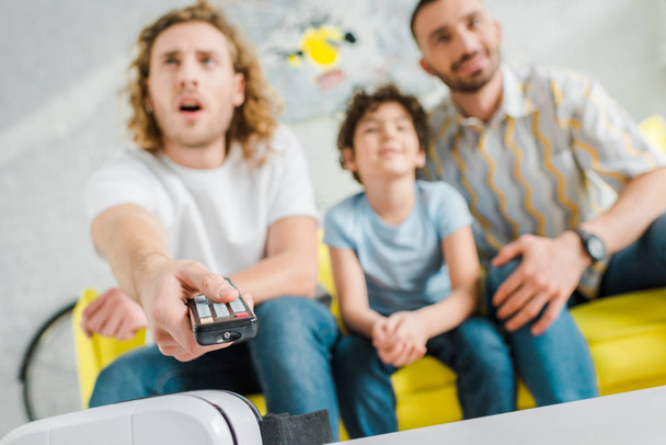selective focus of homosexual parents and mixed race kid watching tv  - Photo, Image