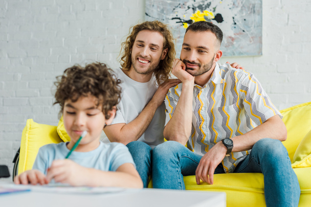 επιλεκτική εστίαση ευτυχείς ομοφυλόφιλοι γονείς κοιτάζοντας μικτή φυλή γιο σχέδιο στο σπίτι  - Φωτογραφία, εικόνα