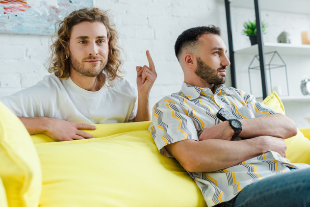 szelektív fókusz elégedetlen homoszexuális férfi mutatja középső ujját partner, miközben filmet néz a nappaliban  - Fotó, kép