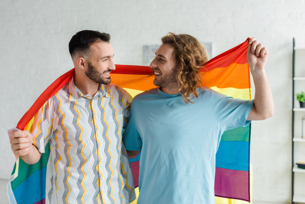 happy homosexual men holding lgbt flag and looking at each other  - Foto, immagini