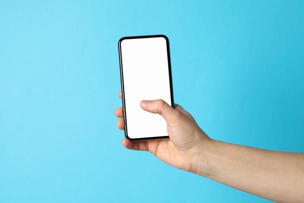 Женщина держит телефон с пустым экраном на синем фоне
 - Фото, изображение