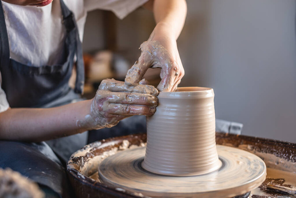 Potter egy fazekas keréken dolgozik, vázát készít. Nő formálja az agyagot kezekkel, kancsót készít egy műhelyben. Közelről. - Fotó, kép