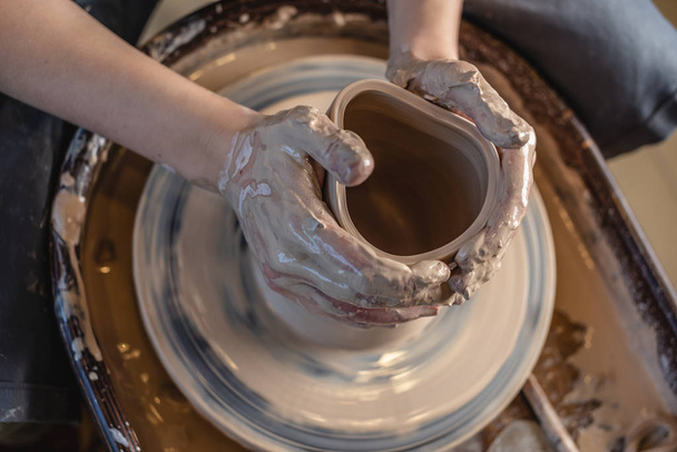 Potter pracuje na Potterově kole a dělá vázu. Žena tvořící hlínu s rukama tvořícíma džbán v dílně. Horní pohled - Fotografie, Obrázek