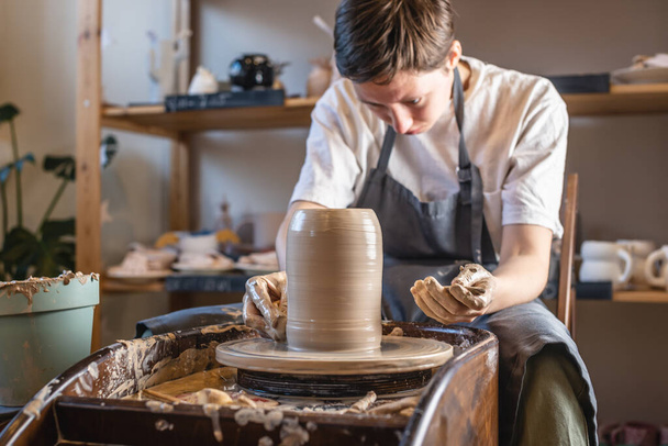 Mujer alfarera trabajando en la rueda de Potter haciendo un jarrón. Maestro formando la arcilla con sus manos creando jarra en un taller
 - Foto, Imagen