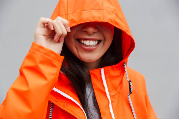 Smiling young asian woman wearing raincoat walking outdoors - Fotó, kép