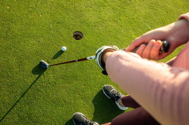 Pretty young woman playing golf on training ground, hits the golf ball into the hole, sport concept - Photo, Image
