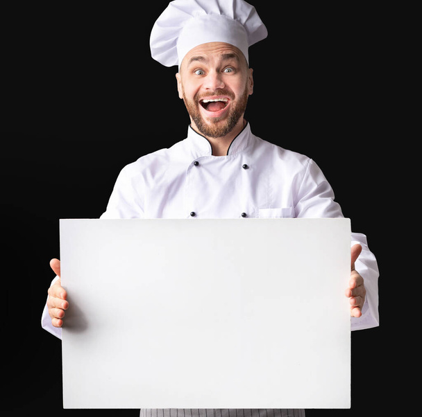 Podekscytowany kucharz trzyma białą tablicę stojącą na czarnym tle - Zdjęcie, obraz