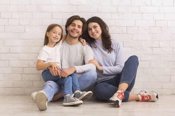 Happy Mom, Dad And Little Daughter Posing Together Sitting On Floor - Фото, изображение