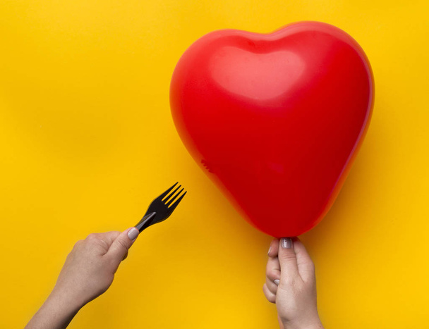 Woman holding red heart balloon and pinned with scissors over yellow - Foto, afbeelding