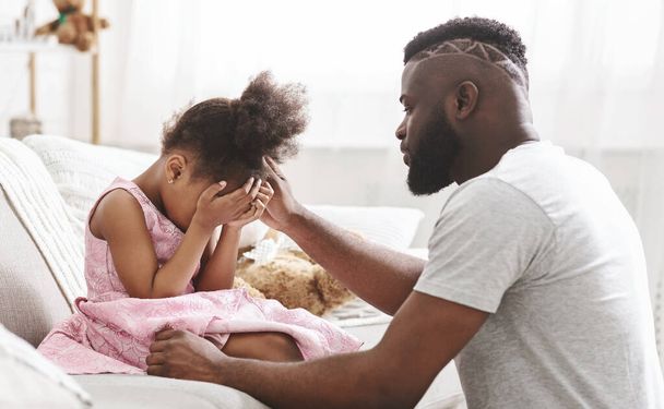 Африканський батько потішає маленьку дівчинку, яка плаче вдома. - Фото, зображення