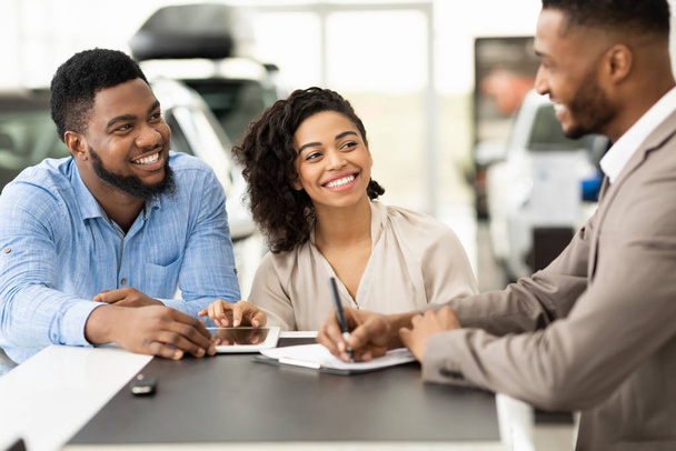 Couple Buying Car Signing Papers With Salesman In Dealership Office - Photo, Image