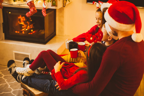 Mañana de Navidad cerca de la chimenea con la familia bebiendo chocolate caliente
 - Foto, Imagen