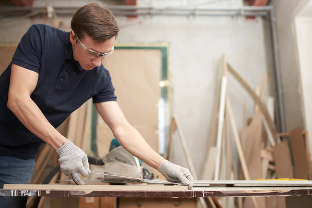 Male carpenter in glasses measures board with centimeter tape in workshop - Foto, immagini