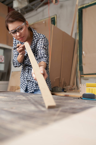 Girl carpenter in glasses with wooden dos and pencil in her hands - Foto, afbeelding