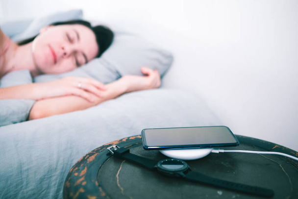 κοιμάται γυναίκα στο κρεβάτι κινητό φόρτιση σε ασύρματο φορτιστή - Φωτογραφία, εικόνα