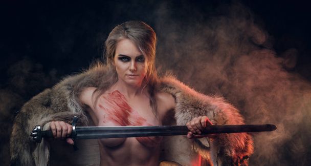 Portrait of a beautiful naked woman with blood stained skin holding a long sword and posing for a camera, wearing only fur. Fantasy fashion. Cosplayer as Ciri from The Witcher - Photo, Image
